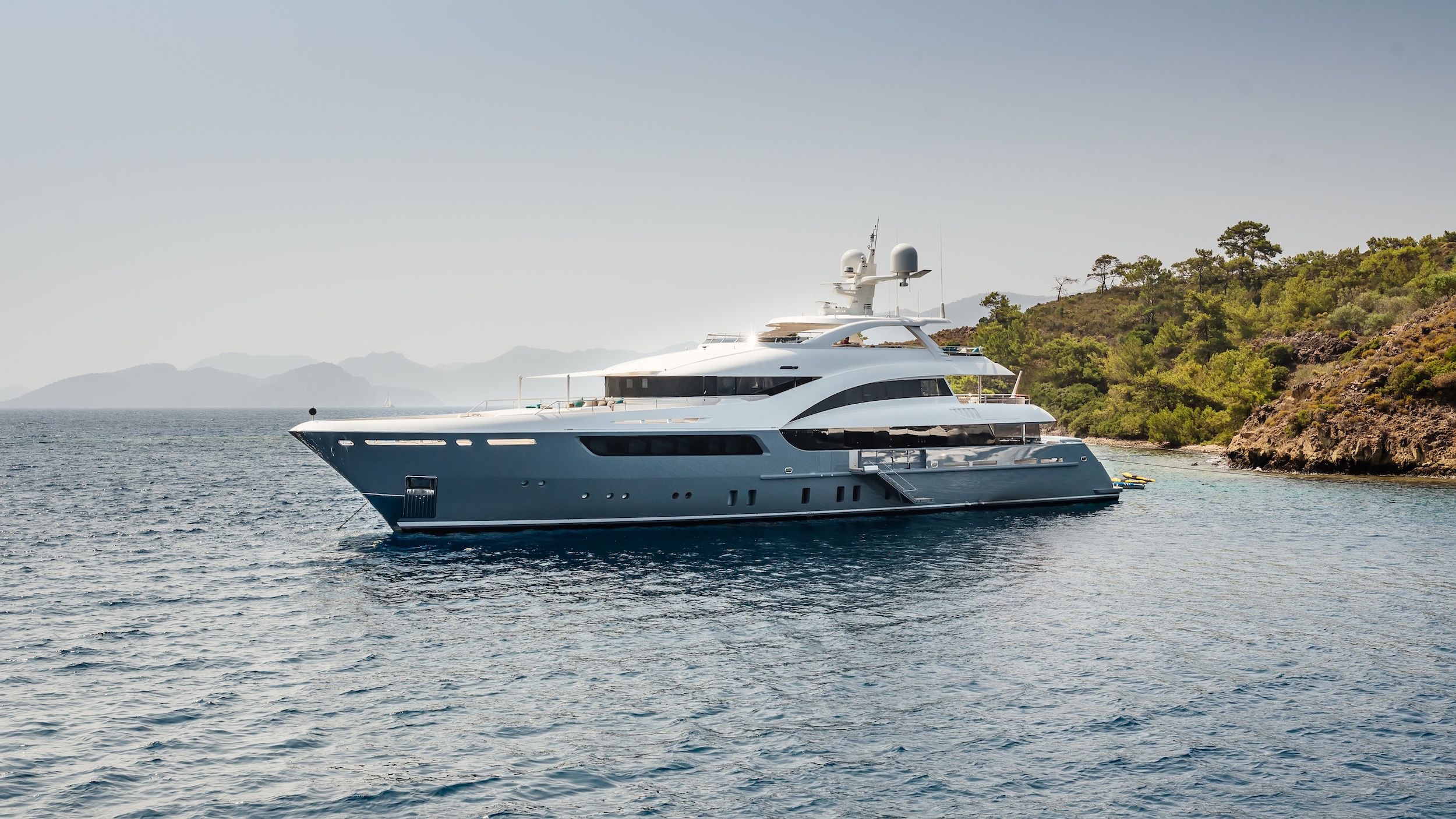 Superyacht at anchor along a rocky coastline